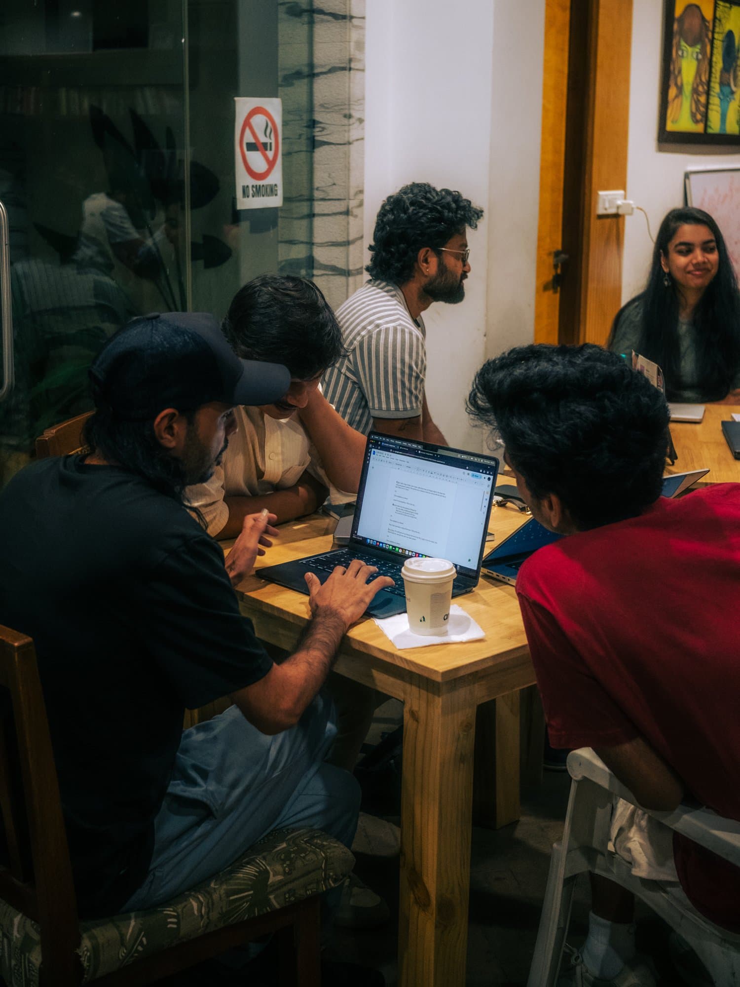 A Writers' Evening group gathered closely around a table with notebooks, laptops, and coffee.