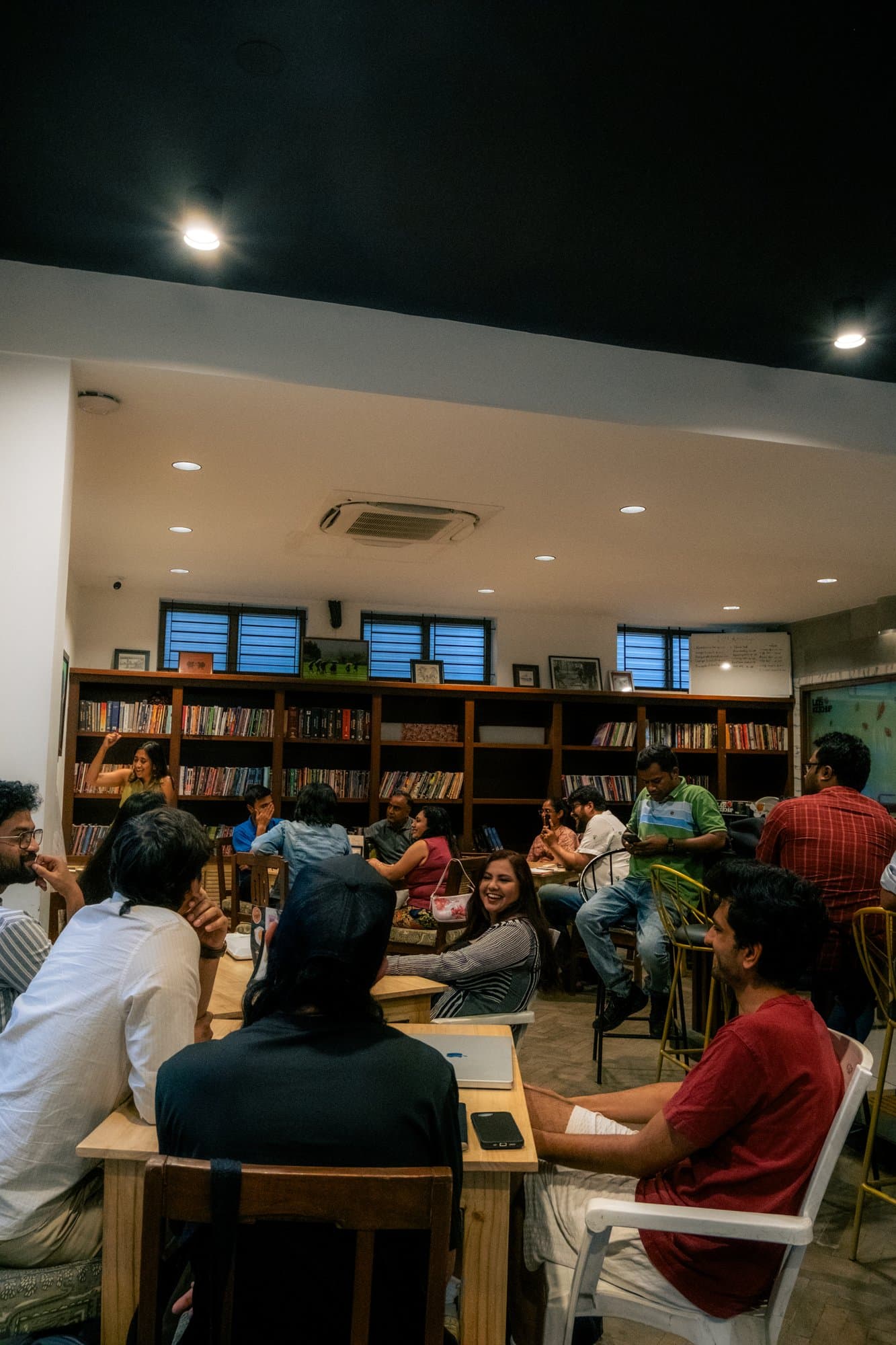 A full Writers' Evening gathering in a book-lined room, with participants seated around several tables.